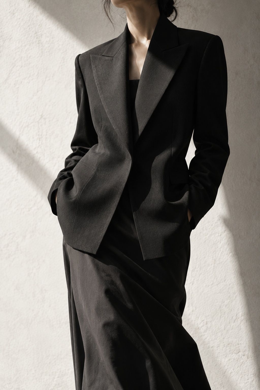 Close crop of a black structured blazer over a long skirt, hands in pockets, cropped at the chin